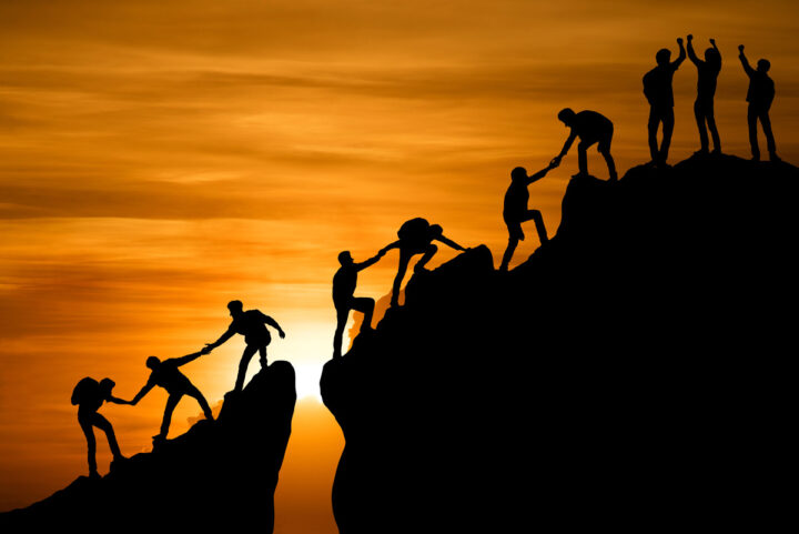 People helping each other to the top of a mountain
