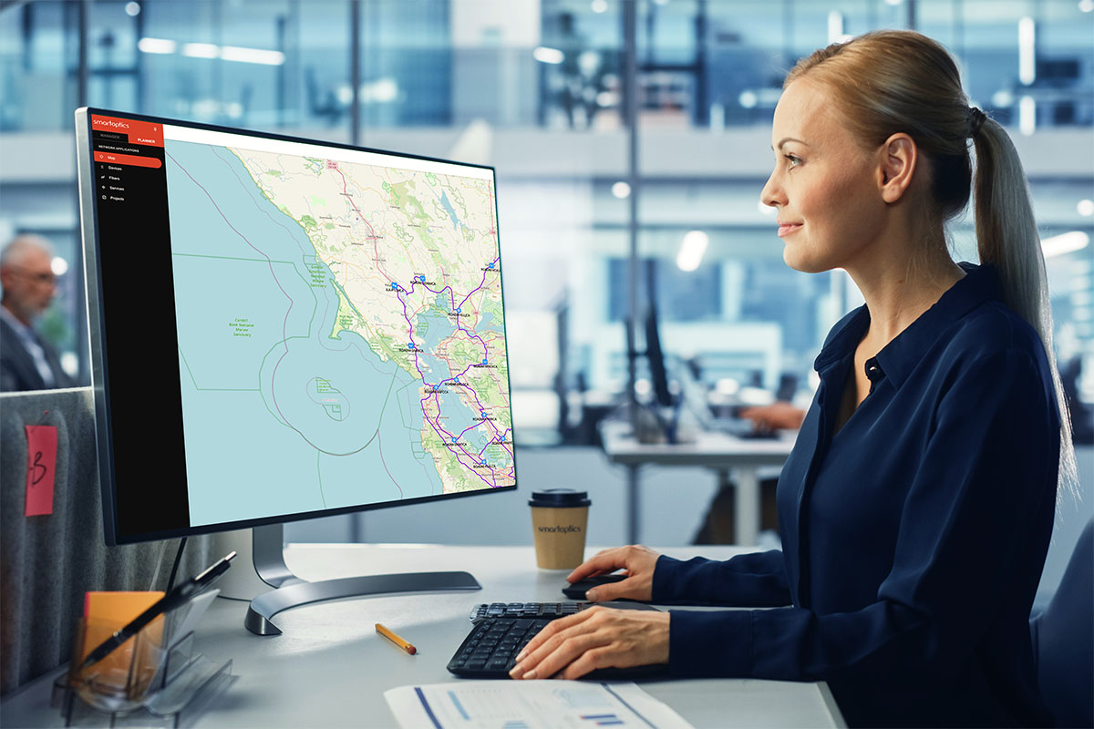 Woman in an office looking at a computer monitor displaying a map with routes and geographic details.